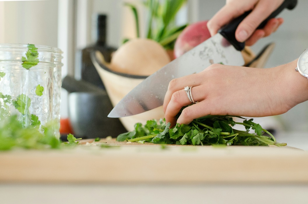 Person chopping vegetables on a wooden cutting board with a sharp knife.