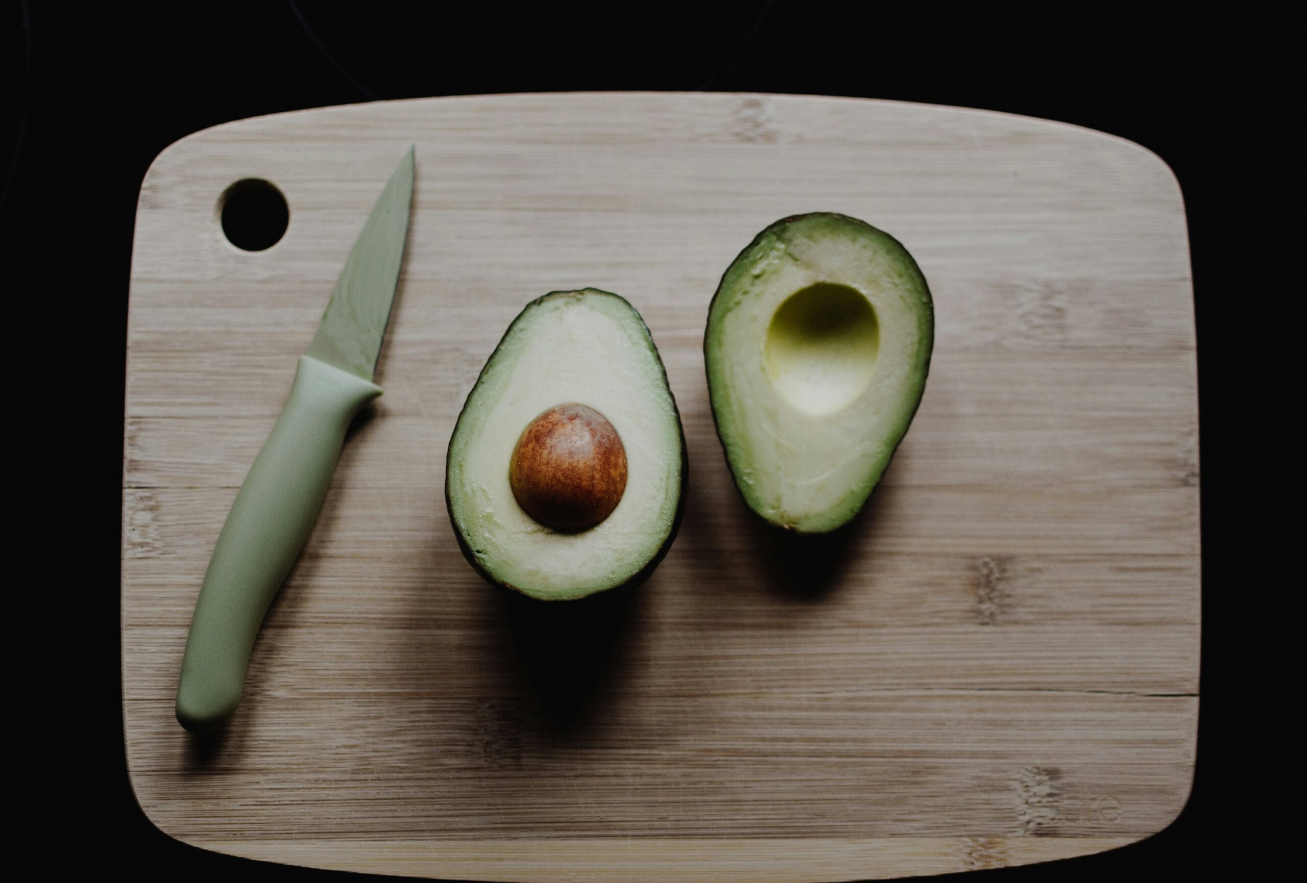 Avocado chopped in half on a chopping board with a knife