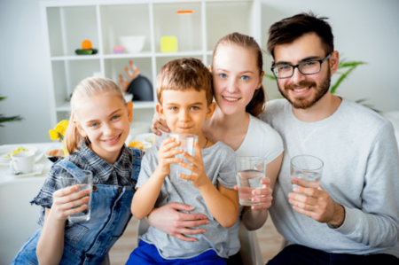 A family of four smiling while holding glasses of water, enjoying a refreshing drink together.