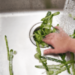 A person washing vegetables in a kitchen sink.