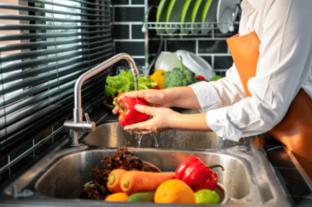 Hands washing a pepper and vegetables over a kitchen sink