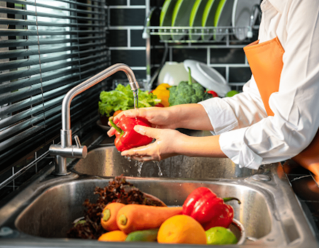 Hands washing a pepper and vegetables over a kitchen sink